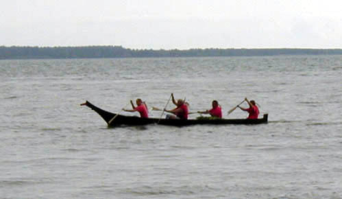 A photo of a taped-seam plywood replica of a Chinook dugout canoe at speed.